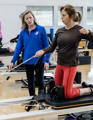 Pilates Reformer class with instructor correcting student's posture