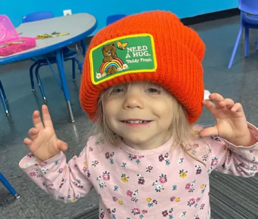 Little girl with a red hat on and arms open wanting a hug