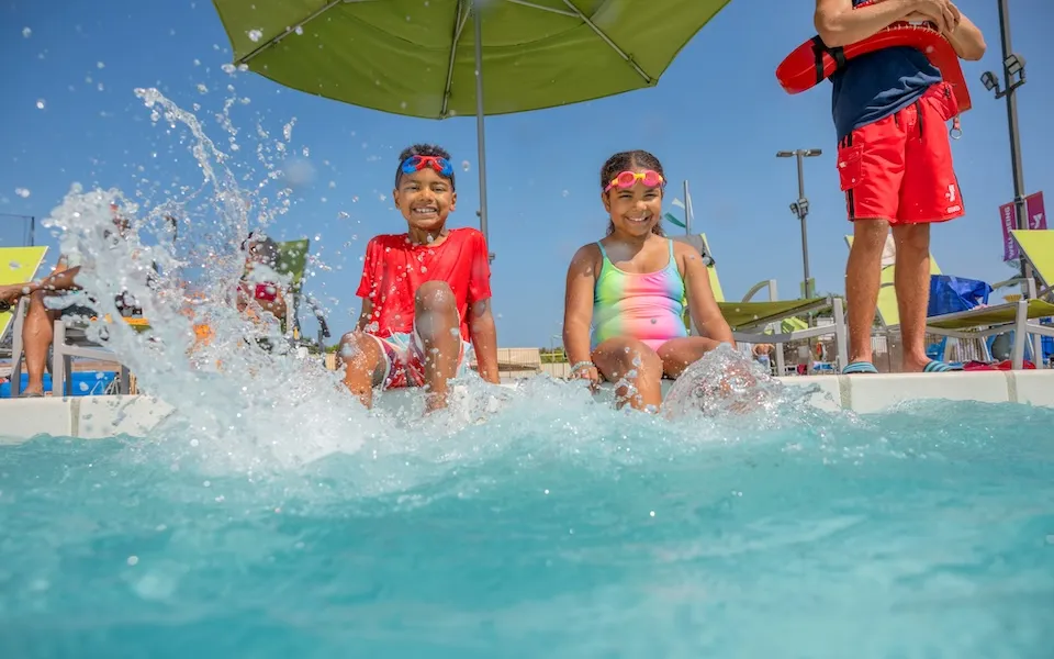 Two kids splashing in the pool at a Safety Around Water class at the Y